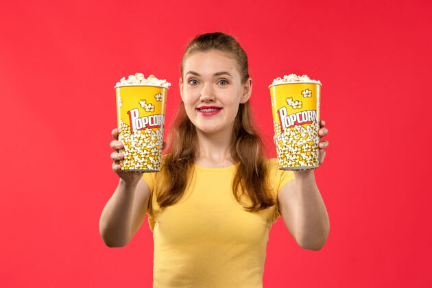 剧院正面图年轻女性在电影院拿着爆米花包在浅红墙电影院里看女性趣味电影电影年轻包装