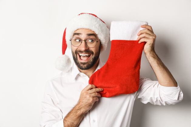 男人特写的快乐男人庆祝圣诞节 收到礼物在圣诞节袜子和期待兴奋 戴圣诞帽和眼镜西装圣诞老人情绪化