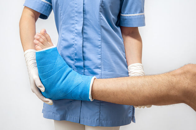腿穿着蓝色医疗袍的女医生正在检查男性患者的断腿瘀伤脚踝骨折