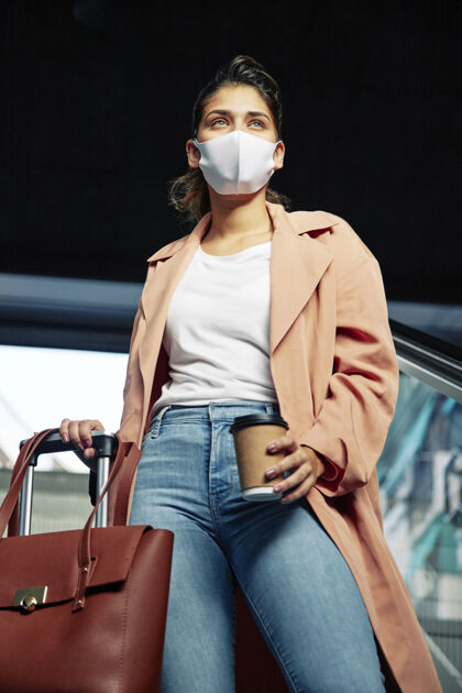 医疗低角度的女人带着医用面罩和行李在机场垂直冠状病毒旅行