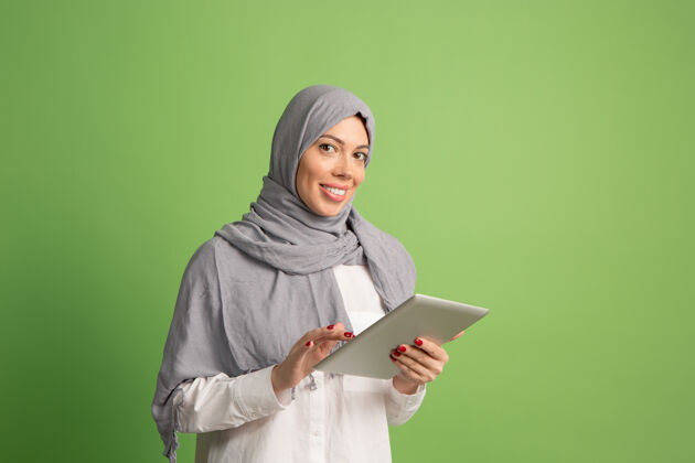 表情戴着头巾的快乐阿拉伯女人带着笔记本电脑微笑女孩的肖像 摆在绿色工作室的背景下年轻感性的女人人类的情感 面部表情概念前视图女孩人宗教