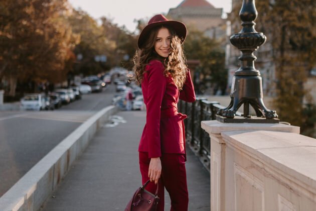 套装笑容可掬的时尚美女身着紫色西装行走在城市街头 春夏秋冬时节时尚潮流戴着帽子 手拿钱包深色阳光优雅
