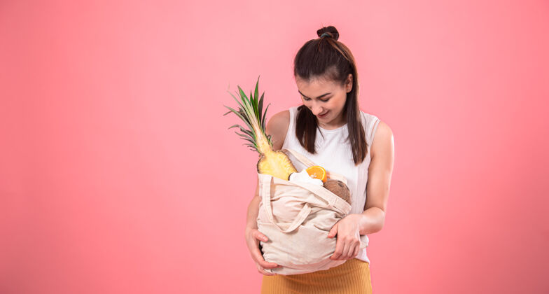 生态时尚的年轻女孩微笑着拿着一个装有异国水果的环保袋购物热带异域风情