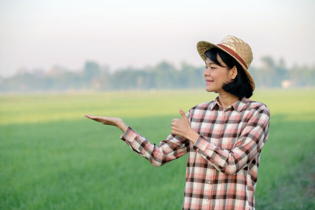 年轻一位亚洲农妇微笑着 在一个绿色的稻田摆出大拇指的姿势农场农业农村