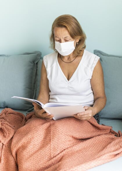 流行病大流行期间带着医用口罩的老太太在家看书防护隔离隔离