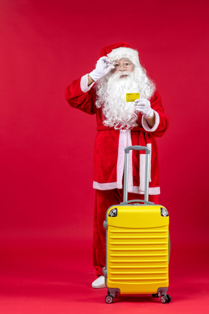 圣诞老人红墙上拿着黄色银行卡的黄色袋子的圣诞老人的正视图圣诞老人快乐举行