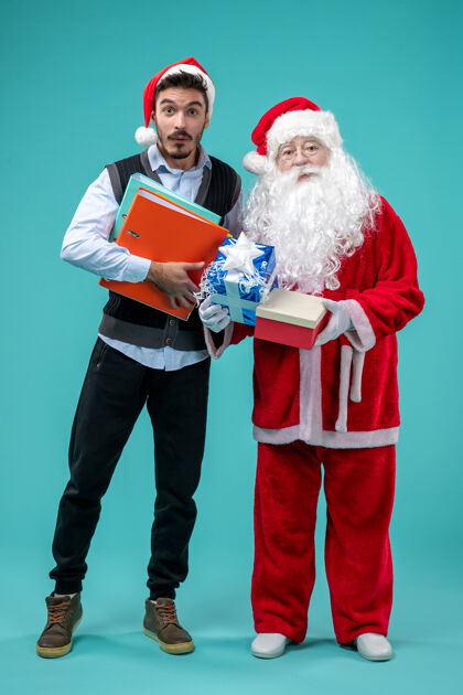 男性圣诞老人与年轻人和礼物在蓝色墙上的正面视图礼物圣诞老人十二月