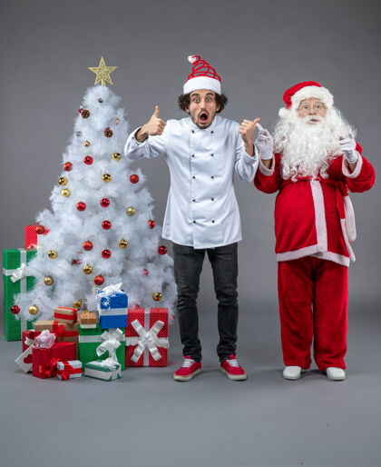 男性圣诞老人和男厨师在灰色墙上围着圣诞礼物的正视图十二月圣诞老人庆祝