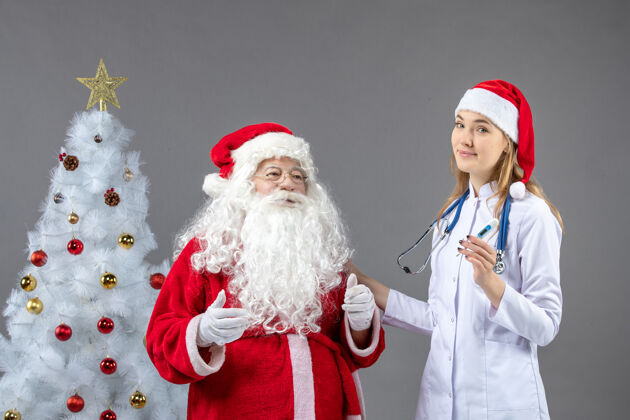 节日圣诞老人和女医生的前视图 女医生拿着测温仪在灰色的墙上圣诞老人女性圣诞节