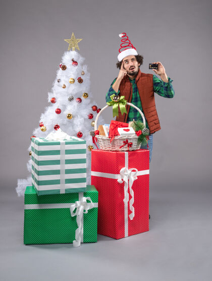 圣诞树年轻的男性在灰色的圣诞礼物周围礼物灰色购物