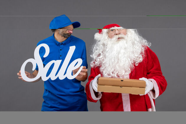 盒子圣诞老人的正面图 男性信使手持销售横幅 灰色墙上有食品盒圣诞老人节日圣诞老人