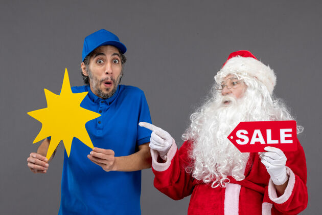 快递圣诞老人的正面图 男信使举着销售横幅 灰色墙上挂着黄色的牌子人圣诞老人男人