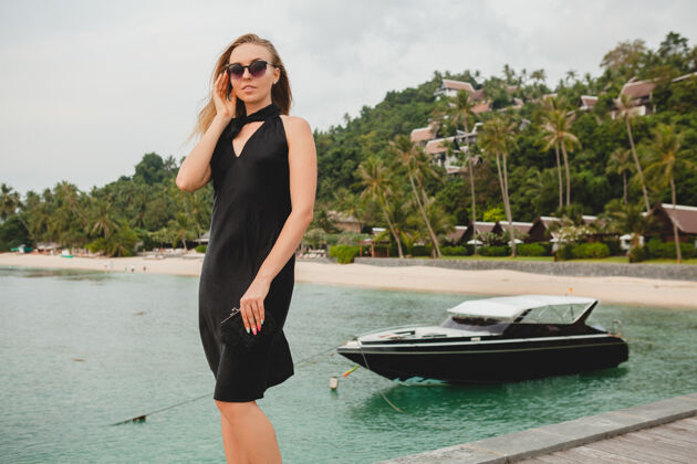 户外奢华性感迷人的女人穿着黑色礼服在豪华度假酒店的码头上摆造型 戴着墨镜 暑假 热带海滩服装休闲女人
