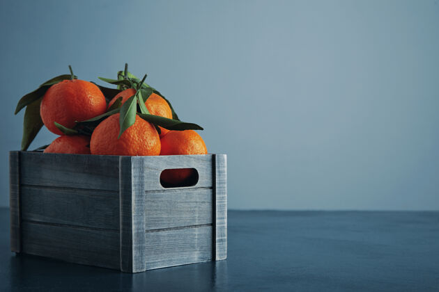 许多新鲜的橘子放在旧盒子里 叶子孤立地放在乡村蓝色的桌子上 冷的背景侧视图特写素食热带橘子