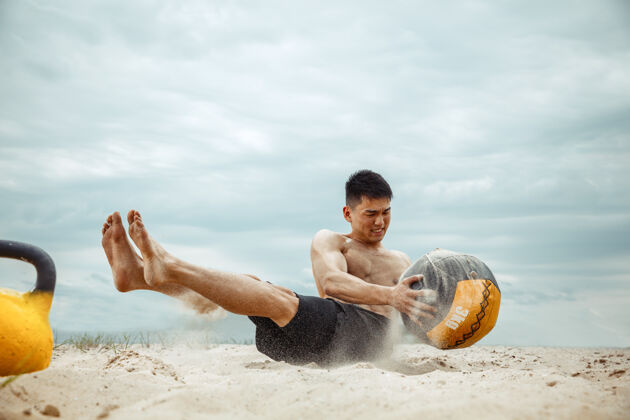 白种人年轻健康的男子运动员在海滩上做深蹲海滩训练年轻