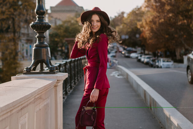 优雅笑容可掬的时尚美女身着紫色西装行走在城市街头 春夏秋冬时节时尚潮流戴着帽子 手拿钱包套装户外女性