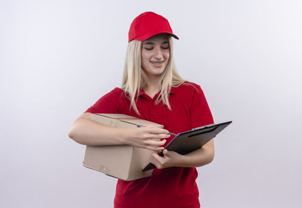 盒子带着微笑的小女孩穿着红色t恤 戴着帽子 戴着牙套 拿着盒子 在剪贴簿上读着孤立的白色背景持有微笑穿着