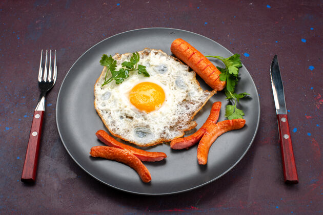 午餐正面图：深色桌子上盘子里放着炒鸡蛋 蔬菜和香肠前面菜绿色