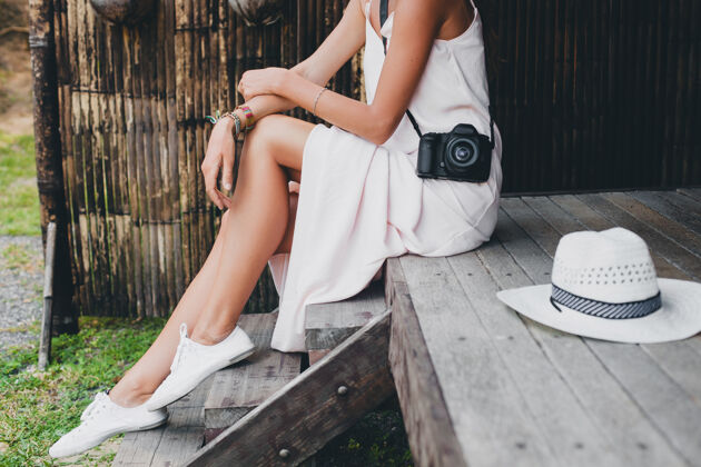 波西米亚人亚洲热带度假的年轻美女 夏季风格 白色波西米亚裙 运动鞋 数码相机 旅行者 草帽 腿部特写细节乐趣模特相机