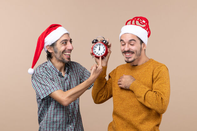米色正面图：两个笑着的男人一个拿着闹钟 另一个在米色孤立的背景上显示时间男成人时间