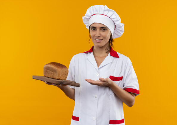 拿面带微笑的年轻女厨师身着厨师制服 手拿面包 手拿面包 放在有复印空间的砧板上切制服板