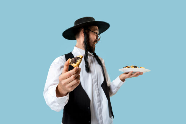 犹太教这位年轻的东正教犹太男子戴着黑帽子 在犹太普瑞姆节上吃哈曼塔森饼干托拉糕点三角形