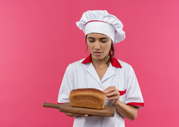 女想着年轻的女厨师穿着厨师制服拿着面包看着砧板上有复印空间拿板子切