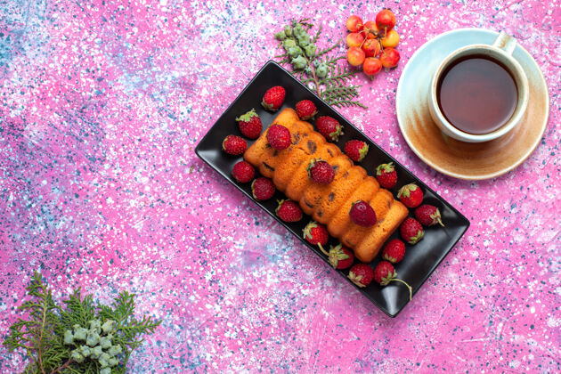 草莓顶视图美味的烤蛋糕放在黑色的蛋糕锅里 粉红色的桌子上放着新鲜的红色草莓新鲜糖红色