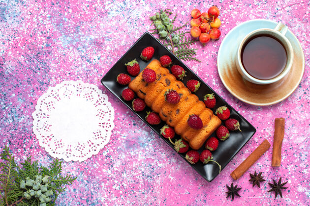 蛋糕顶视图美味的烤蛋糕放在黑色蛋糕锅里 粉红色的桌子上放着新鲜的红色草莓和茶茶饼干烘焙