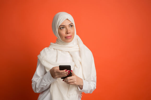 微笑戴着手机头巾的快乐阿拉伯女人微笑女孩的肖像 摆在红色工作室的背景下年轻感性的女人人类的情感 面部表情概念前视图表情肖像