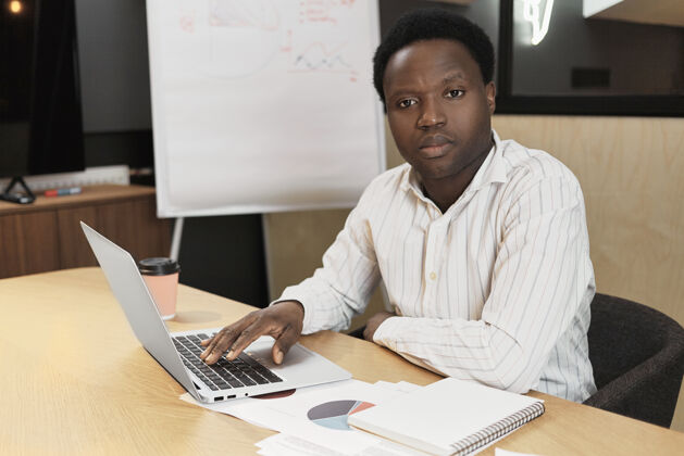 表情英俊自信的年轻黑皮肤男性坐在书桌旁拿着文件专注专业人士衬衫
