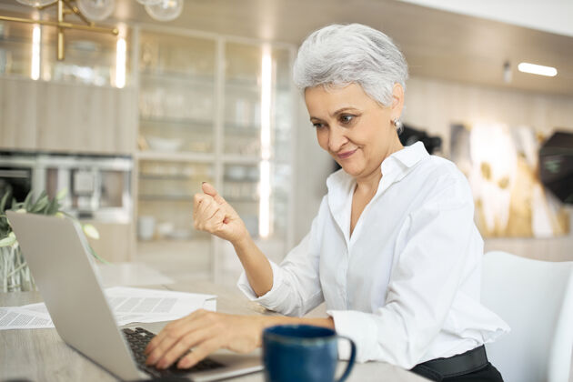 成功成熟的女商人使用笔记本电脑进行远程工作 坐在办公桌前喝咖啡愤怒手势女性
