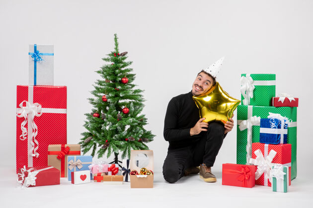 礼物正面图：年轻人围坐在礼物旁边 拿着金色的星形枕头 微笑着站在白色的墙上圣诞节节日抱着