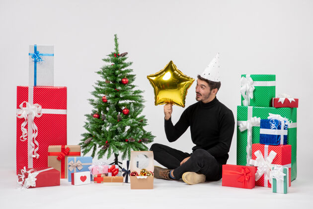 节日年轻人围坐在礼物旁边 拿着金星在白墙上圣诞快乐人坐着