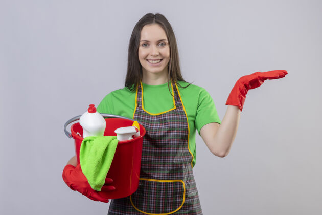年轻微笑的清洁年轻女孩穿着制服 戴着红色手套 手持清洁工具 在孤立的白色背景上举手女孩白微笑