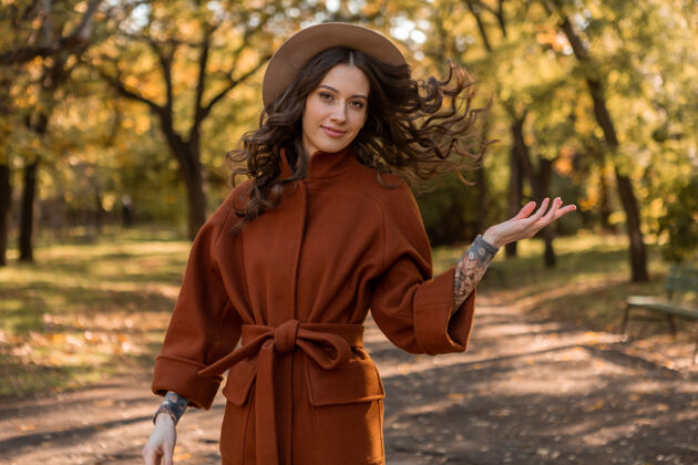 休闲美丽时尚的微笑瘦身女子卷发漫步公园身着温暖的棕色外套 秋日时尚街头风苗条欢快漂亮