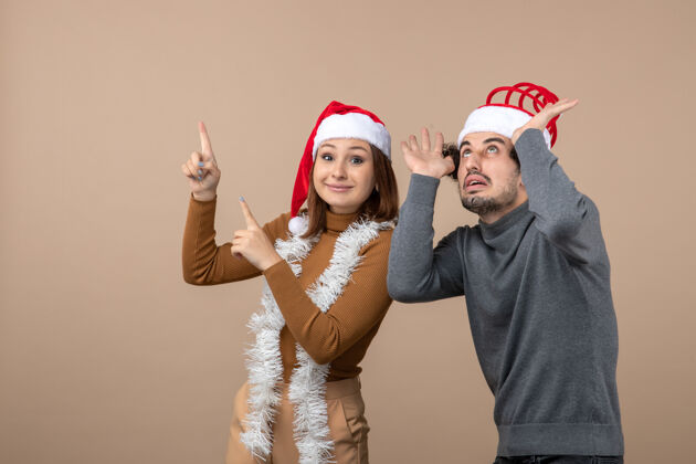 红色圣诞节心情激动凉爽满意可爱情侣戴着红色圣诞老人帽指着上方可爱的情侣满意心情