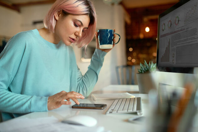 女士侧视图时尚的粉红色头发的年轻女博客坐在桌前的台式电脑智能手机女商人早晨