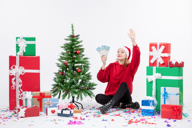 坐着前视图年轻女子围坐在白墙上拿着飞机票的礼物圣诞节前面快乐