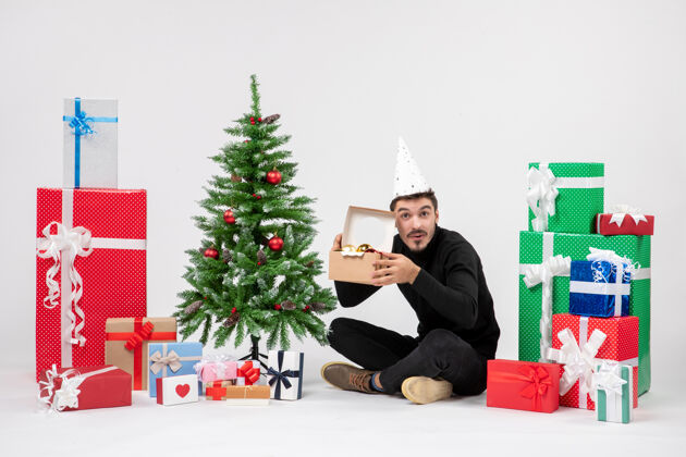 礼物正面图：年轻人围坐在节日礼物旁边 手里拿着白色墙上的玩具包人快乐人
