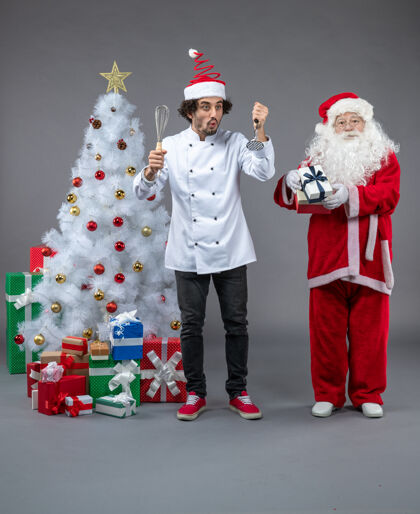 帽子圣诞老人和男厨师在灰色墙上围着圣诞礼物的正视图圣诞老人男性圣诞快乐