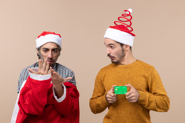 两个朋友前视图两个朋友一个背对前圣诞老人外套 另一个信用卡米色孤立的背景外套风景朋友