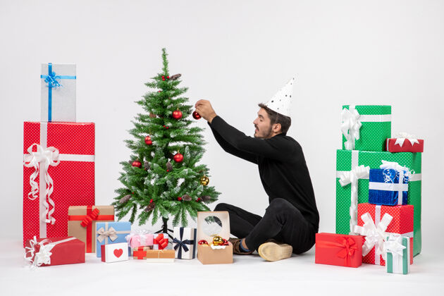 快乐年轻人围坐在节日礼物装饰白色墙上的小树的前视图圣诞快乐节日人