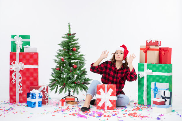 情感年轻女子围坐在礼物和白色墙上的小圣诞树前的视图圣诞树女人节日