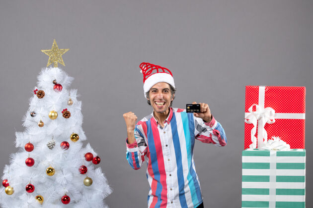 举行前视图兴高采烈的男子手持卡片靠近白色圣诞树灰色树卡片
