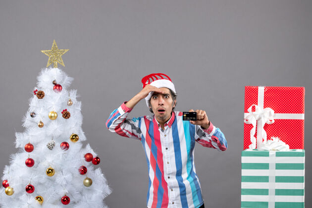 圣诞前视图：一个站在白色圣诞树旁的男人把手放在额头上人天真观察