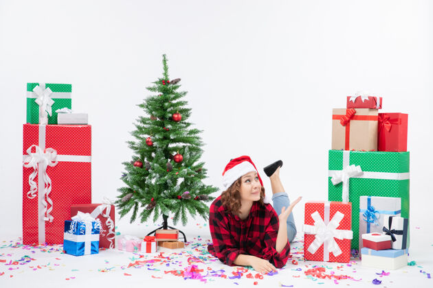 礼物前视图年轻的女性躺在圣诞礼物和小圣诞树周围 背景是白色的女人给新年的圣诞雪涂上颜色年轻礼物周围