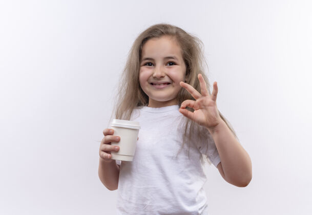 杯子微笑的小女生穿着白色t恤 手里拿着一杯咖啡 在孤立的白色背景上显示出良好的姿态好的咖啡微笑