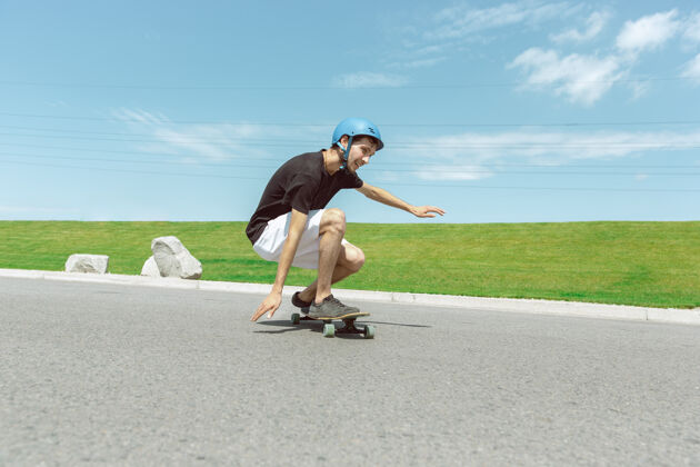 跳跃在阳光明媚的日子里 在城市街道上玩滑板的人年轻人在草地附近骑马 玩长板休闲活动 运动 极限 爱好和运动的概念沥青游戏速度