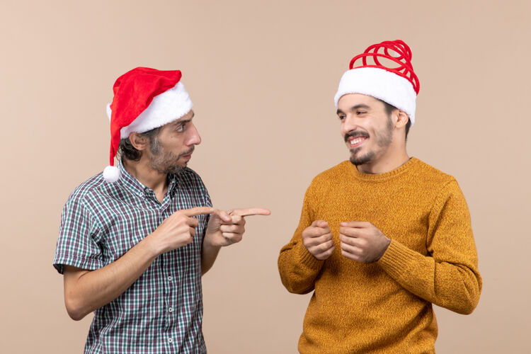 伙计们前视图两个戴圣诞帽的家伙 一个手指在米色孤立背景上展示另一个观点帽子观点